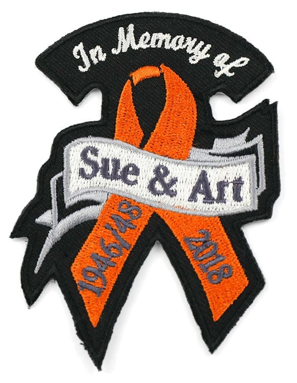 Black, white, orange, and gray embroidered patch, hot cut to ribbon shape: In Memory of Sue and Art, 1946 to 2018